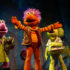 A colorful cast of Fraggles dances across the stage, surrounded by bright set pieces and playful lighting, bringing the joy, music and imagination of Fraggle Rock to life.